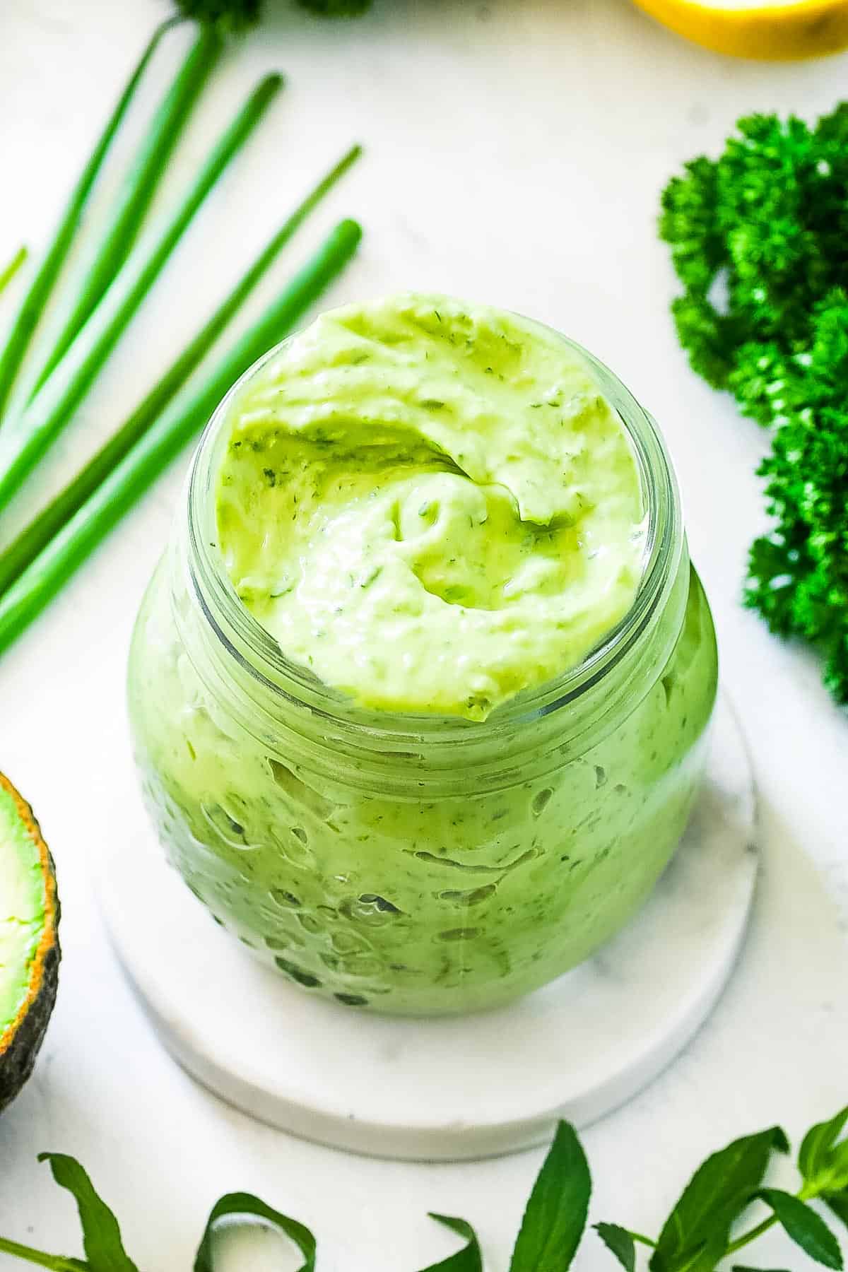 Close-up image of the green goddess avocado dressing served in a small gl، jar. 