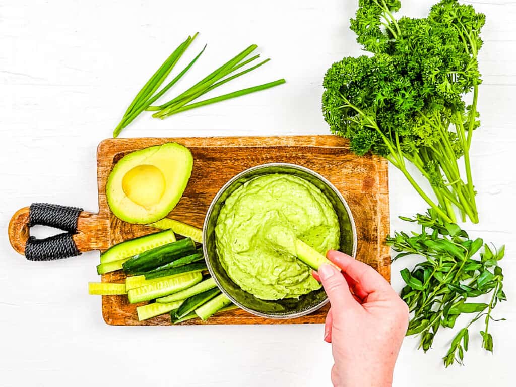 Dipping a cucumber stick into thick creamy green goddess avocado sauce.