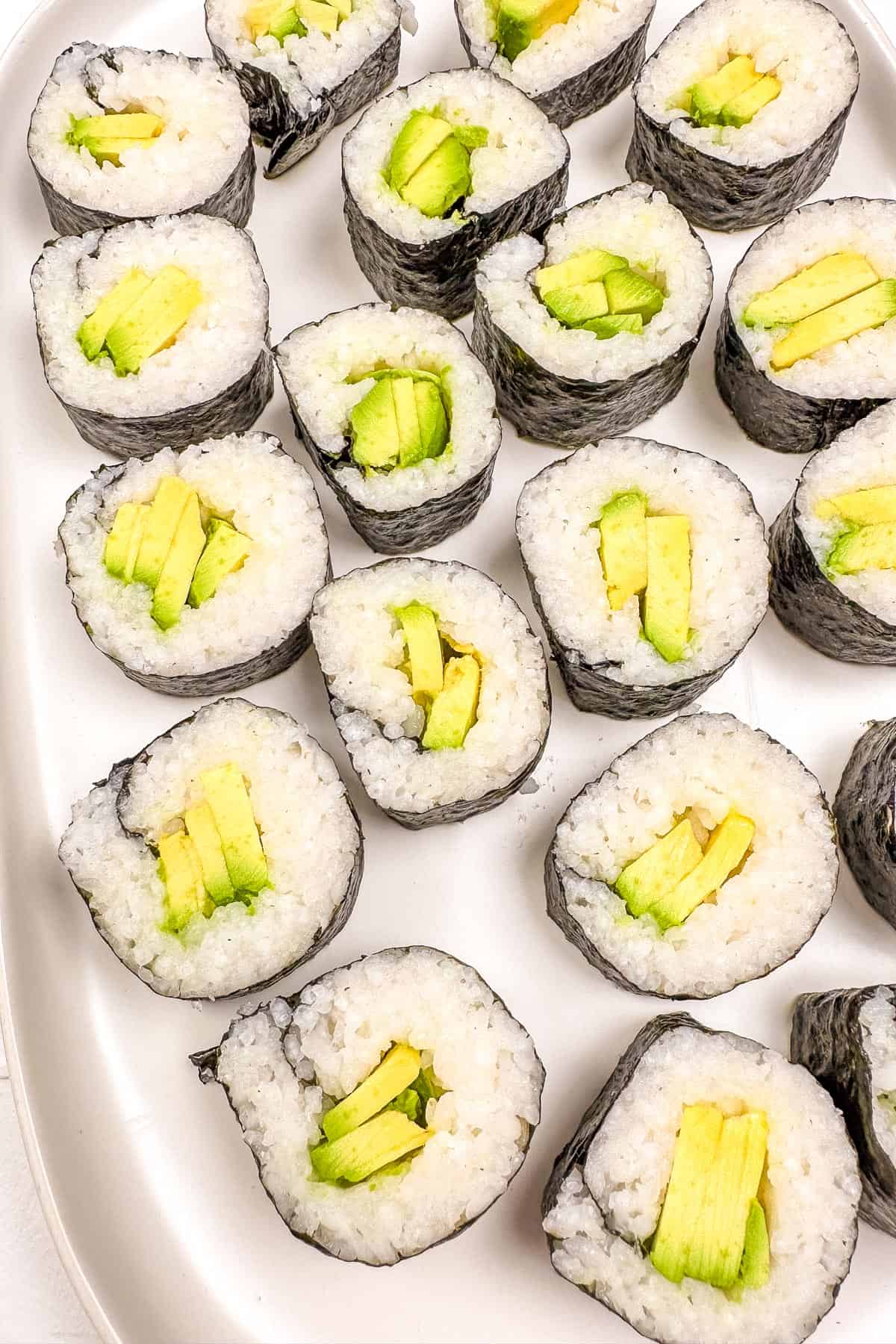 Sliced avocado sushi rolls laid out on a white plate.
