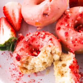 Baked strawberry donuts on a white plate with fresh strawberry slices.