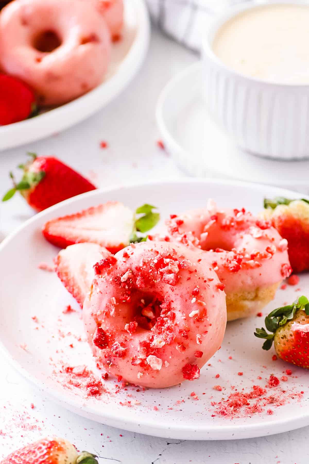 Baked strawberry donuts on a white plate surrounded by fresh strawberry slices.