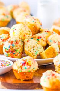 Birthday cake muffins, stacked on a white plate with sprinkles on the side.