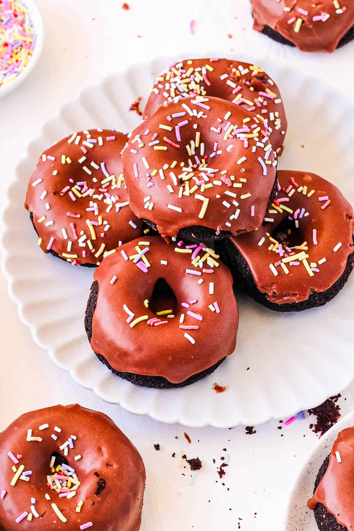 A pile of chocolate donuts served on a white plate.