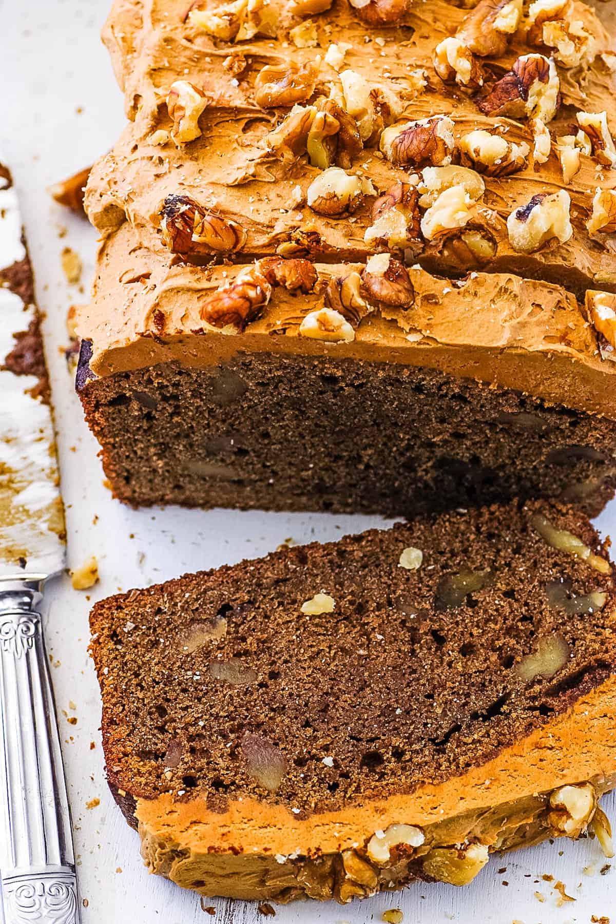 Coffee and walnut loaf cake with coffee icing, sliced on a white cutting board.