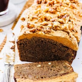 Coffee and walnut loaf cake with coffee icing, sliced on a white cutting board.