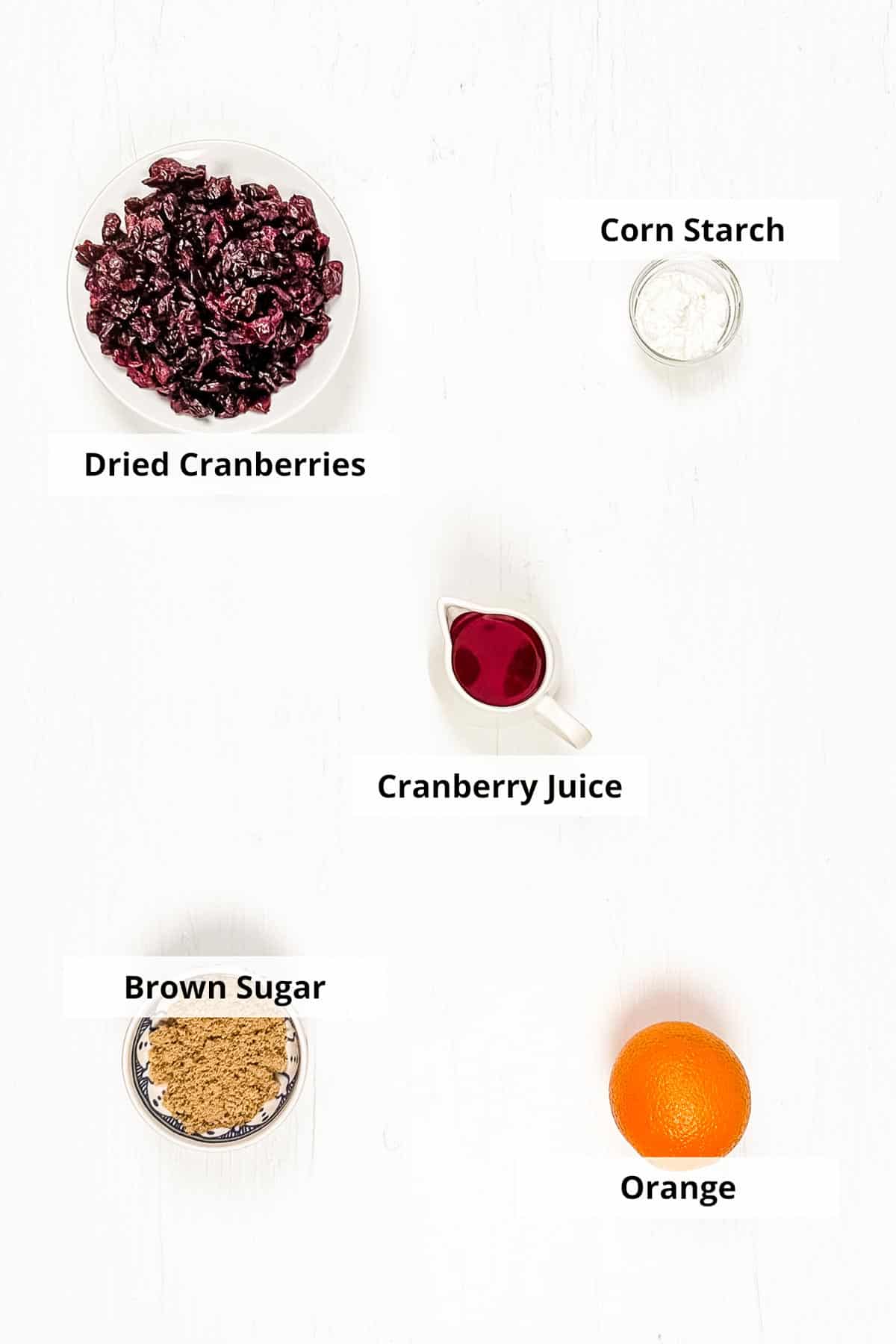 Ingredients for the dried cranberry sauce laid out in small ceramic dishes on a white background.