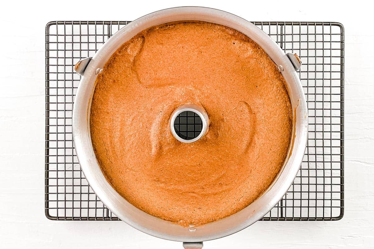 Baked angel food cake in the cake tin cooling on a wire rack.