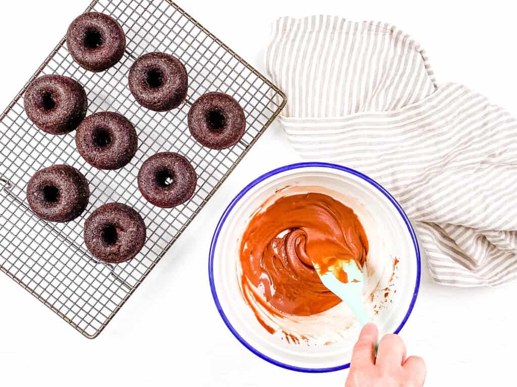 Adding the chocolate topping to the donuts on a wire cooling rack.