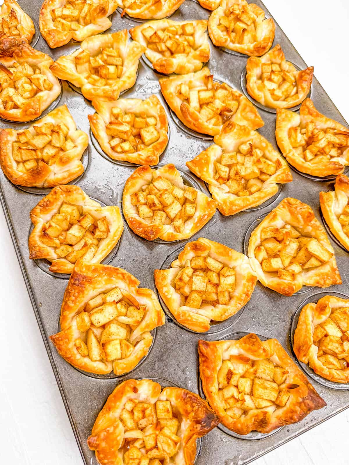 Baked mini apple pies in the muffin tray before being removed to cool.