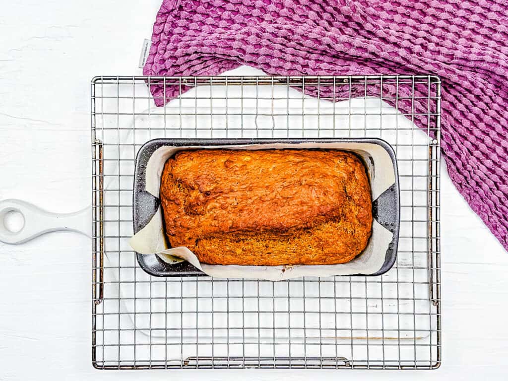 Baked healthy banana pumpkin bread in a loaf pan, cooling on a wire rack.