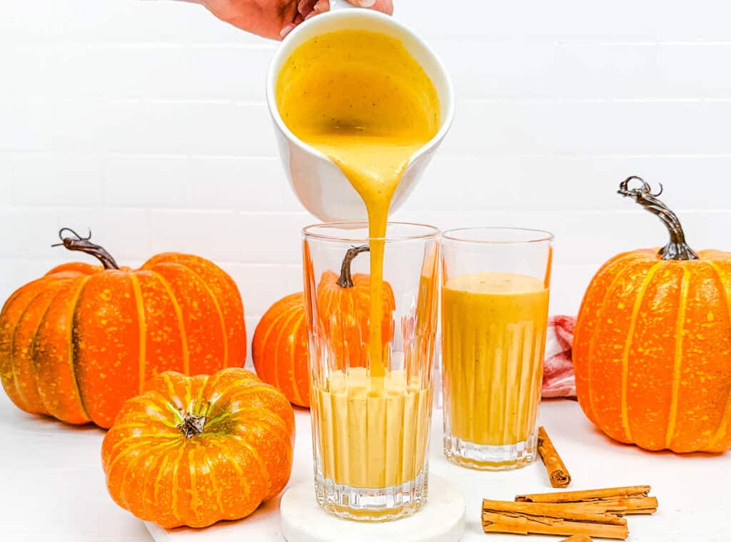 Pumpkin pie smoothie being poured into glasses on a white countertop.