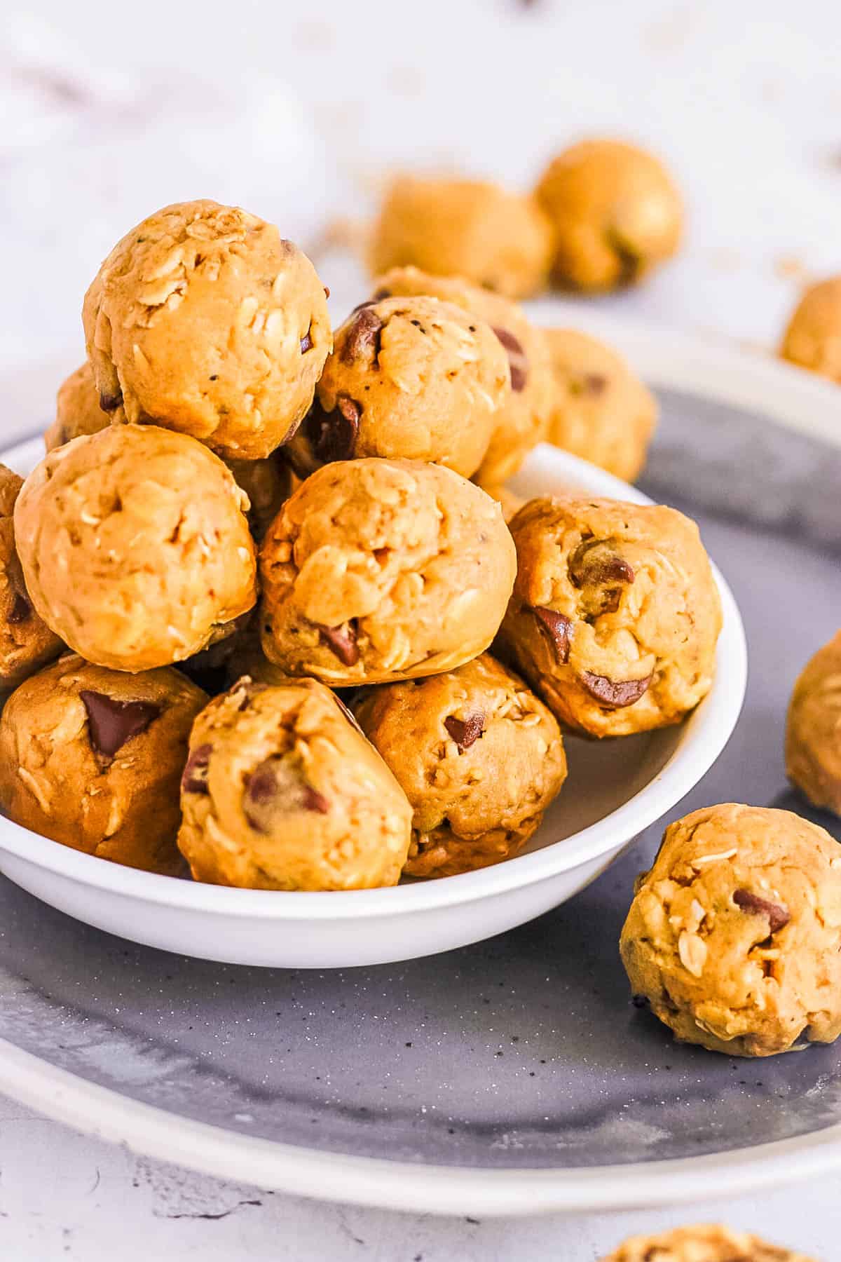 Stack of vegan protein balls made with peanut butter, oats, protein powder, and chocolate chips, in a white bowl.