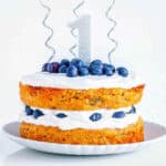Healthy vegan smash cake topped with blueberries and vegan frosting with 1st birthday decorations on top.