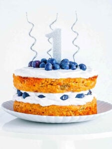 Healthy vegan smash cake topped with blueberries and vegan frosting with 1st birthday decorations on top.