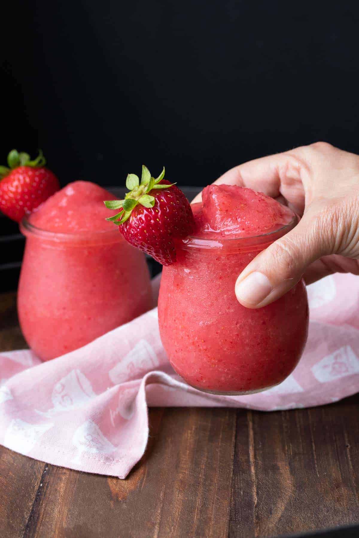 Hand holding a glass of bright pink frose drink.