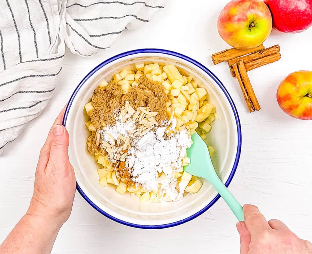 The apple pie filling is being mixed in a large mixing bowl.