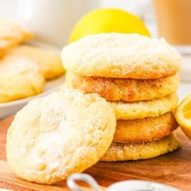 A stack of lemon biscuits with one biscuit leaning on the stack from the side, on a wooden board.