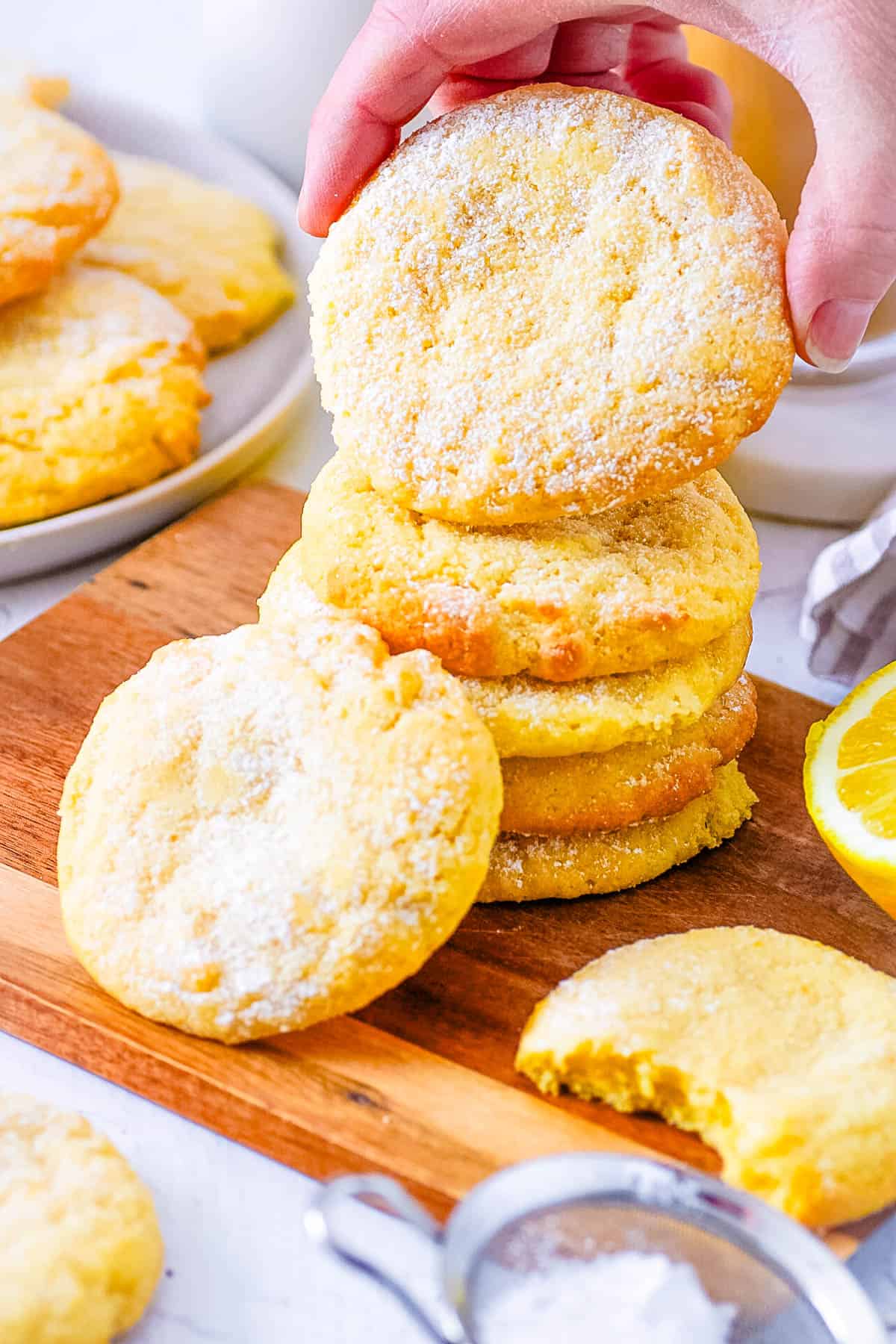 A hand picking up a lemon biscuit from a pile of cookies on a wooden board.