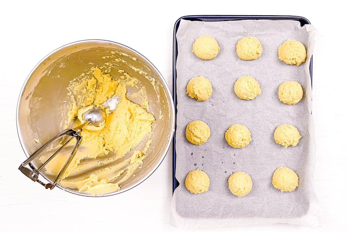 Scoops of lemon cookie dough laid out on a metal baking sheet lined with parchment paper.