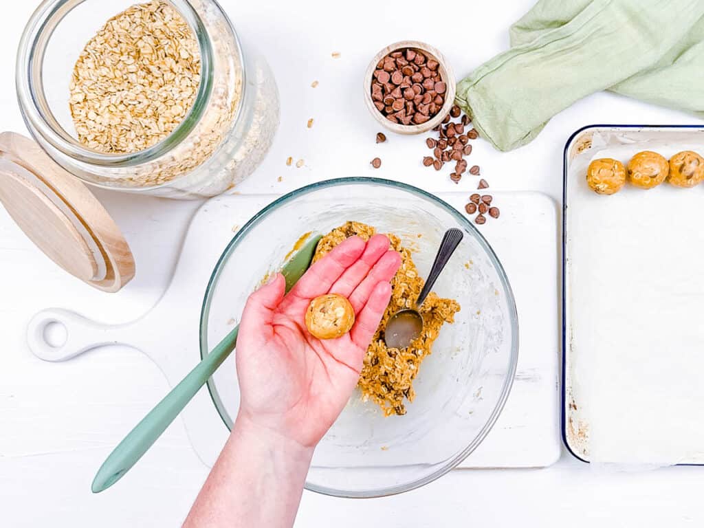 Hand rolling a vegan energy bite on top of a mixing bowl.