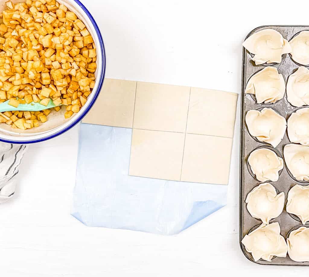 The puff pastry being cut into small squares before being pushed into the ،in tin.