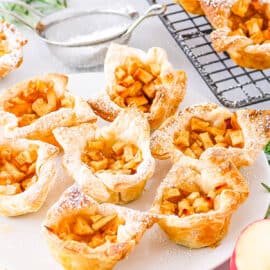 Flaky mini apple pies with puff pastry served on a white plate and dusted with powdered sugar.