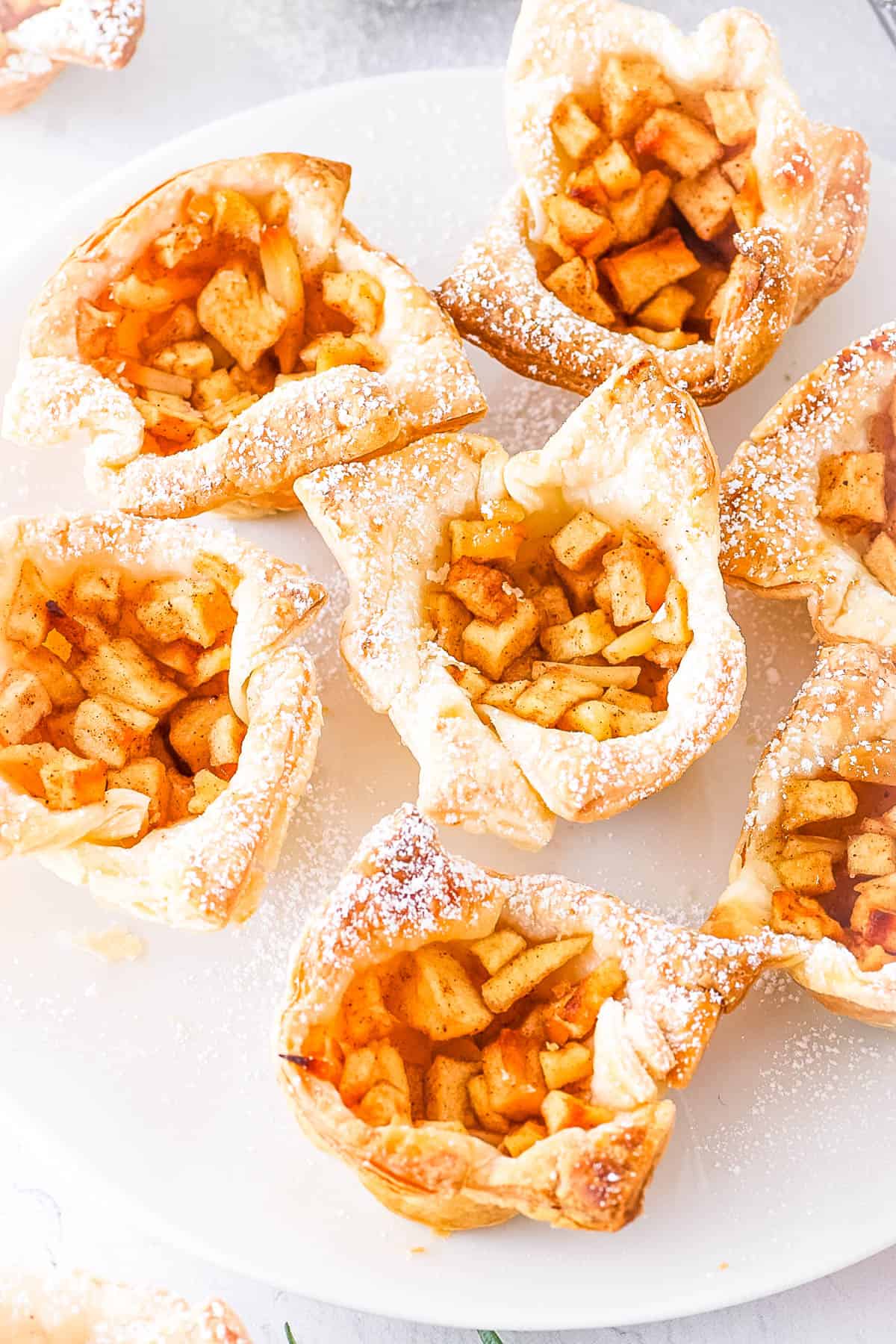 Mini apple pies dusted with confectioners sugar served on a white plate.