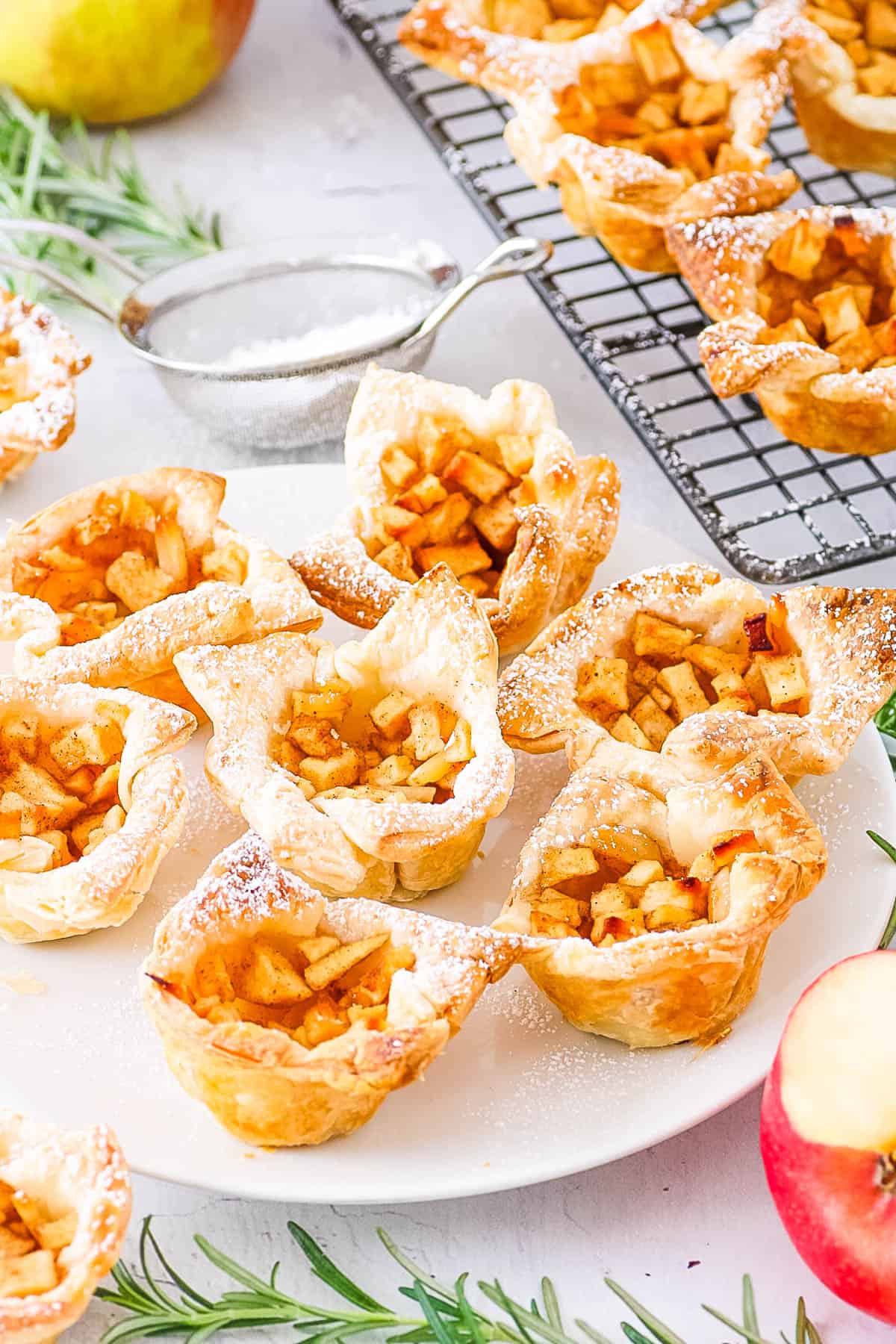 Flaky mini apple pies with puff pastry served on a white plate and dusted with powdered sugar.