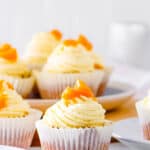 Peach cupcakes, topped with a vanilla buttercream frosting and stewed peaches, on a white plate.