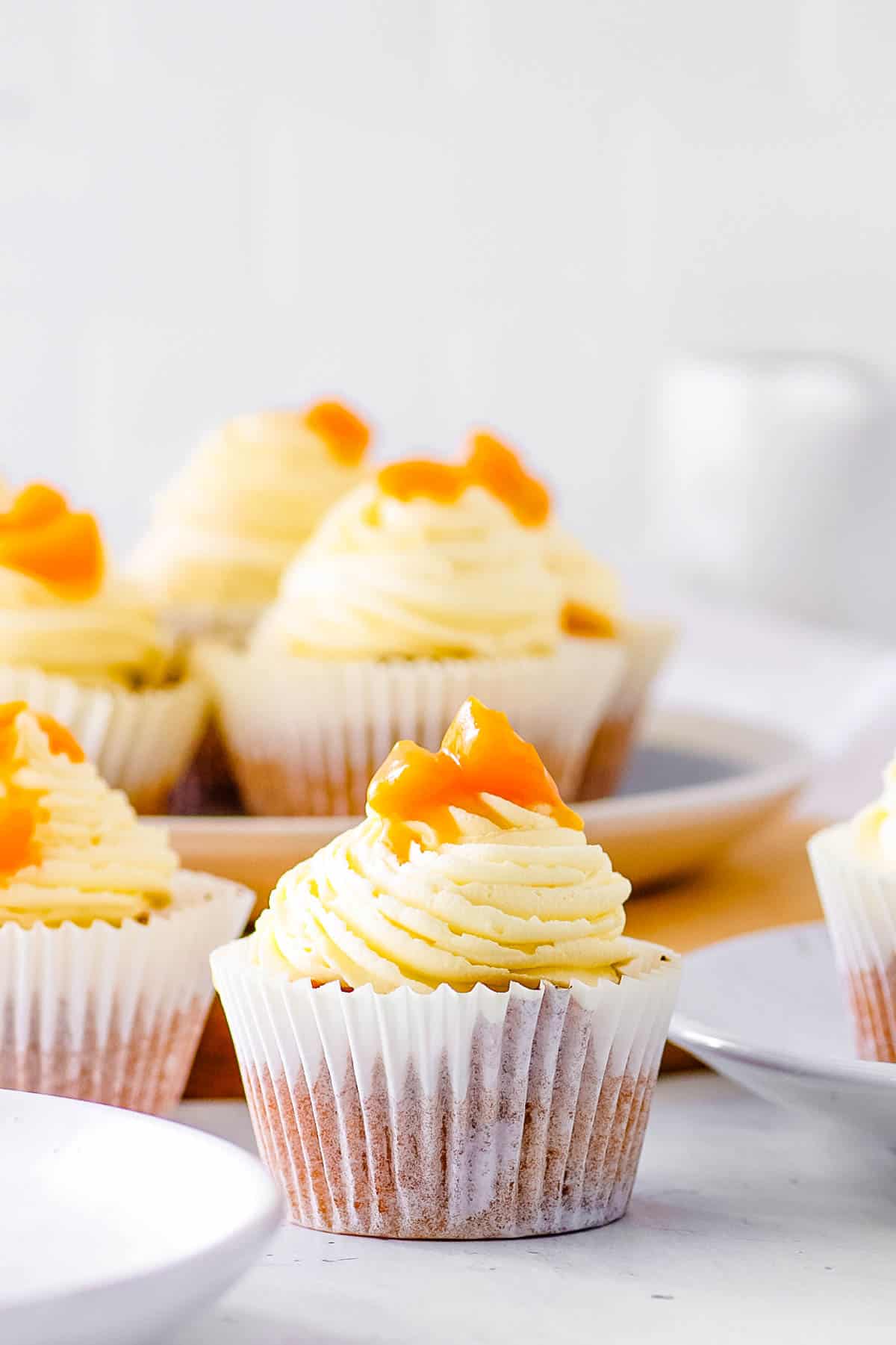 Peach cupcakes, topped with a vanilla buttercream frosting and stewed peaches, on a white plate.