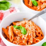 A bowl of pink sauce pasta served with fresh basil and grated parmesan cheese.