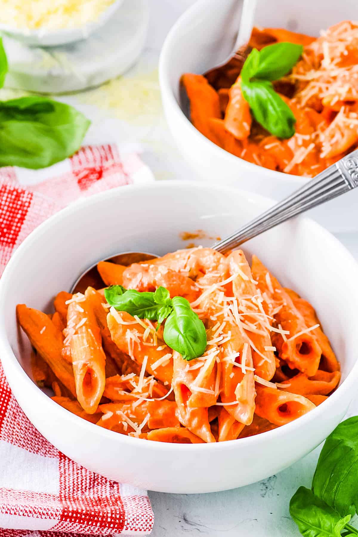 A bowl of pink sauce pasta served with fresh basil and grated parmesan cheese.