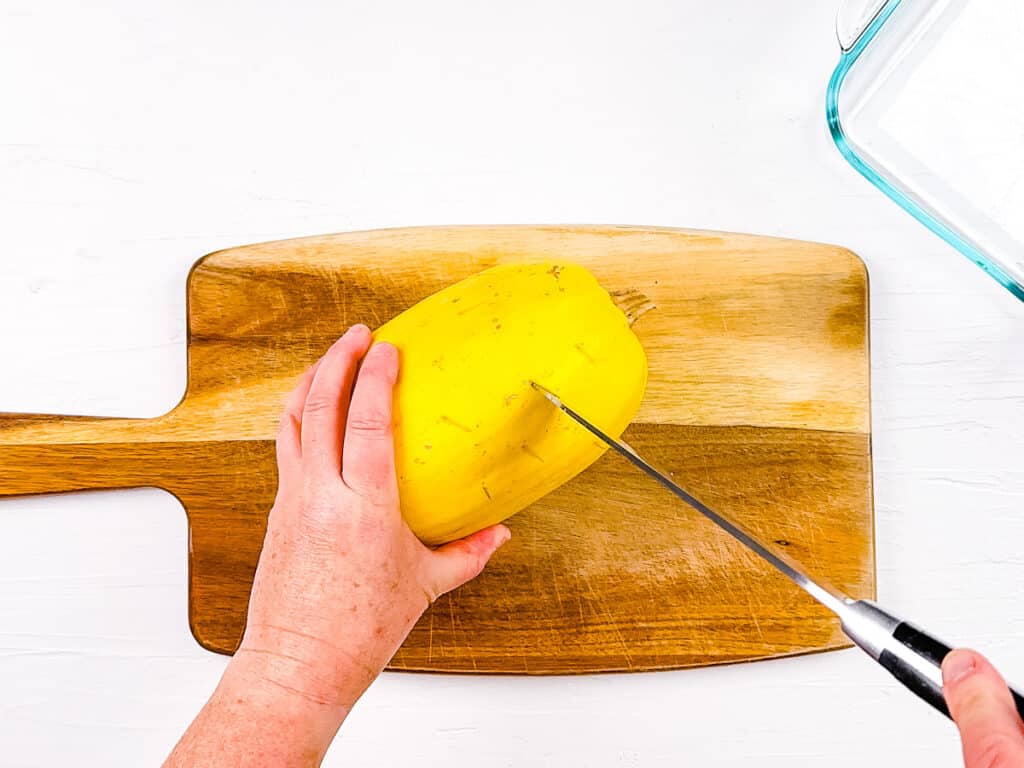 Spaghetti squash being cut on a cutting board.