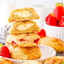A stack of strawberry cheesecake cookies stacked on top of one another with fresh strawberries in the background.