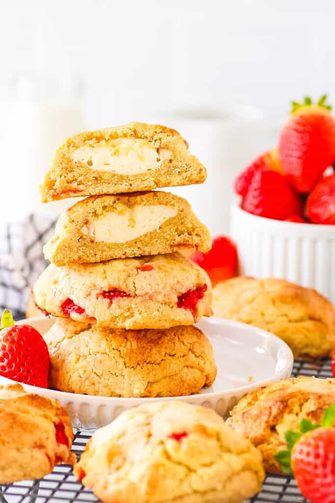 A stack of strawberry cheesecake cookies stacked on top of one another with fresh strawberries in the background.