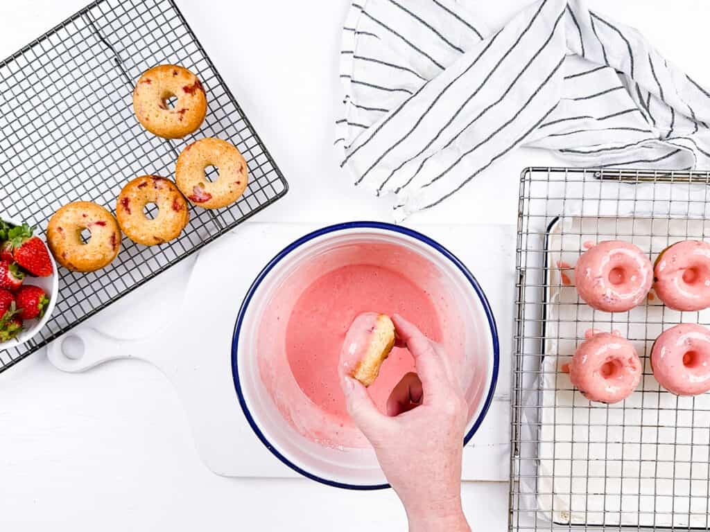 Dipping baked strawberry donuts in strawberry glaze.