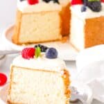 A slice of angel food cake on a white plate with whipped cream and fresh berries and a spoon.