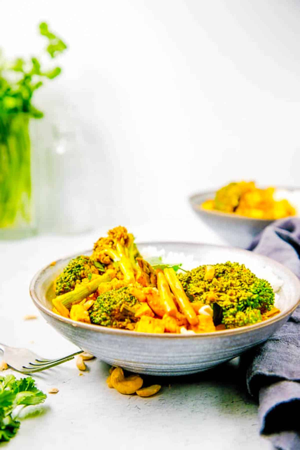 Tofu Thai yellow curry with broccoli, ،atoes, asparagus and peppers served in a grey bowl.