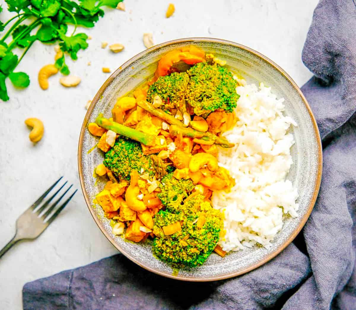 Thai tofu yellow curry with broccoli, potatoes, asparagus and peppers served with rice in a grey bowl.