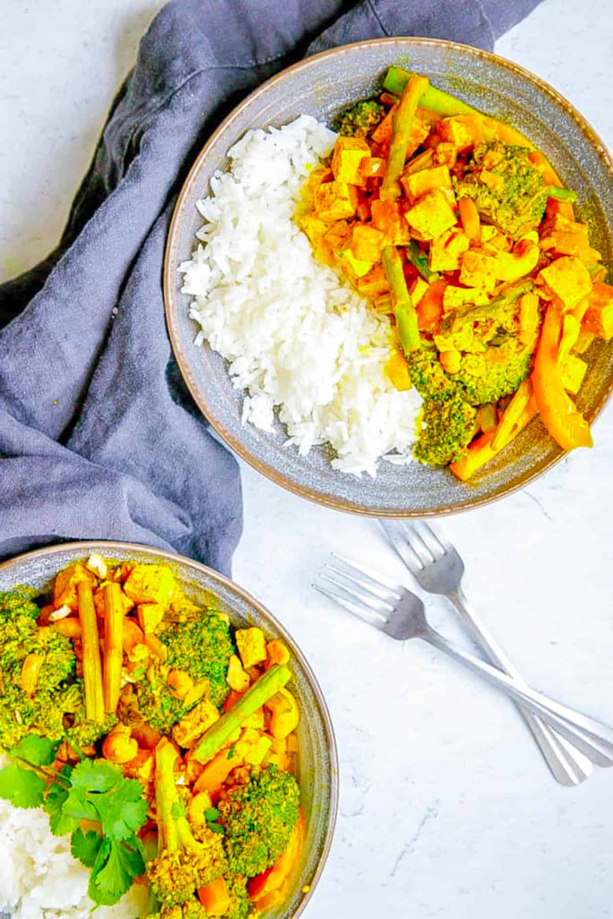 Tofu Thai yellow curry with broccoli, potatoes, asparagus and peppers served in a grey bowl.