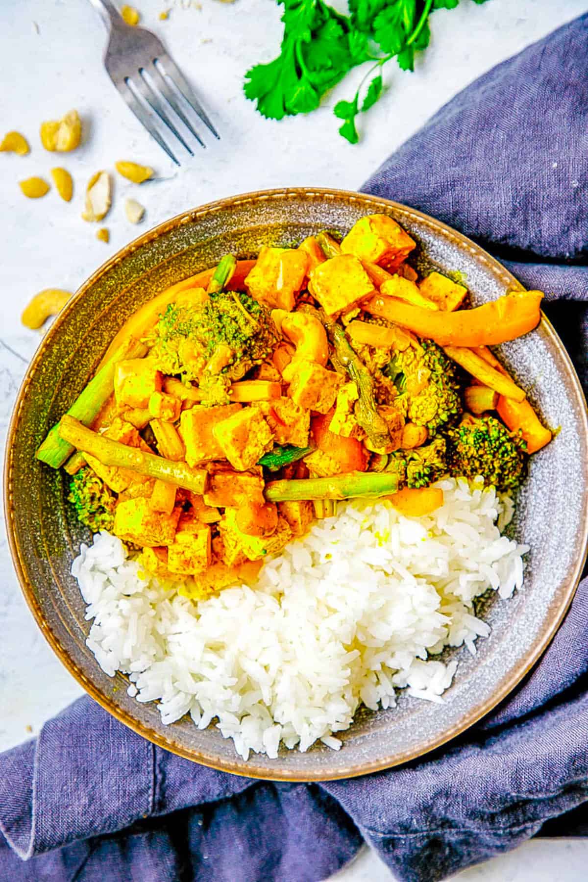Thai tofu yellow curry with broccoli, ،atoes, asparagus and peppers served in a grey bowl.
