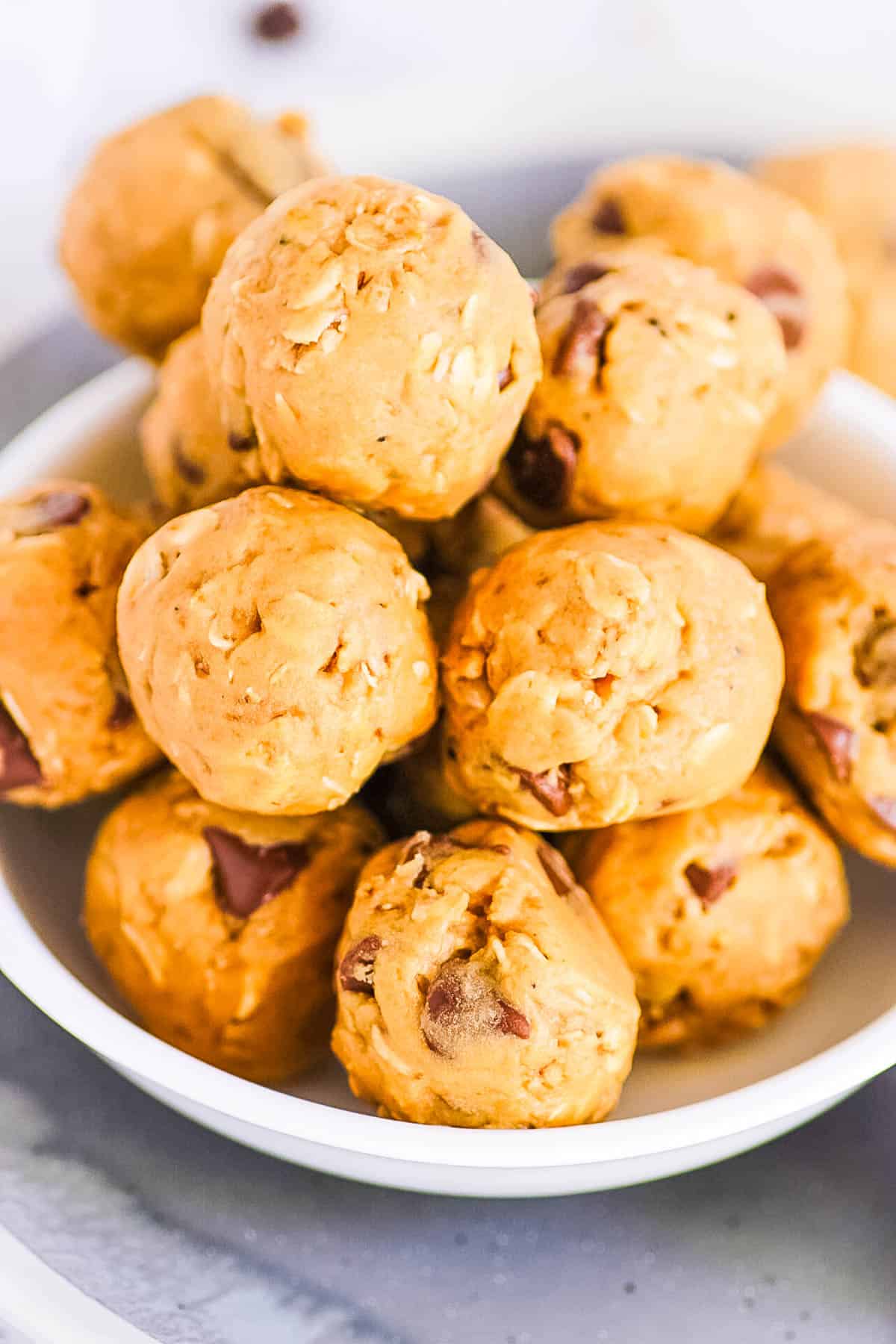 Stack of vegan protein balls made with peanut butter, oats, protein powder, and chocolate chips, in a white bowl with a hand picking up one ball.