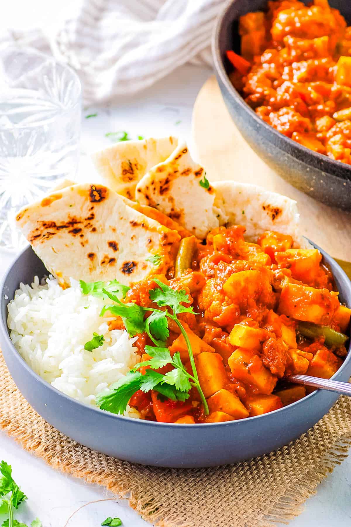 Vegetable vindaloo served in a bowl with naan and rice on the side.