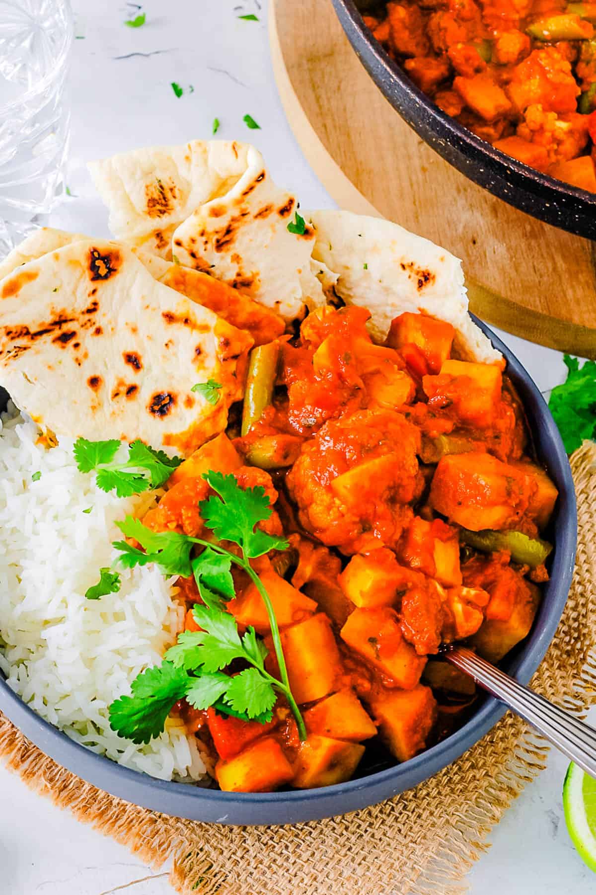 Vegetable vindaloo served in a bowl with naan and rice on the side.