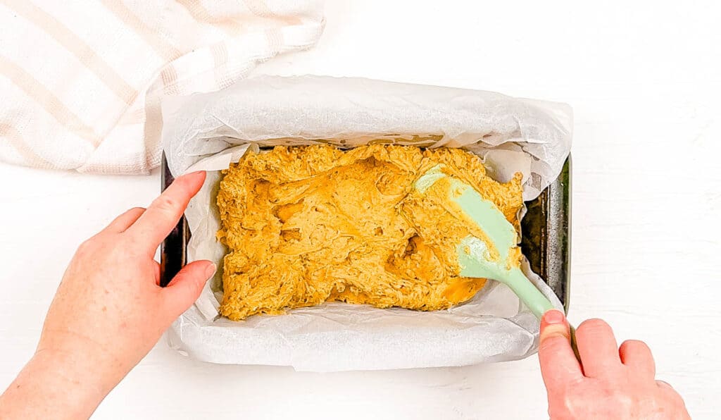 Cake batter spread into a loaf pan lined with parchment paper.