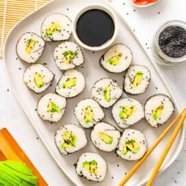 A large white platter with sliced avocado sushi rolls laid out with soy sauce and pink ginger.