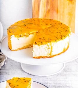 Slice of passionfruit cheesecake on a plate with whole cheesecake in the background.