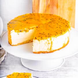 Slice of passionfruit cheesecake on a plate with whole cheesecake in the background.