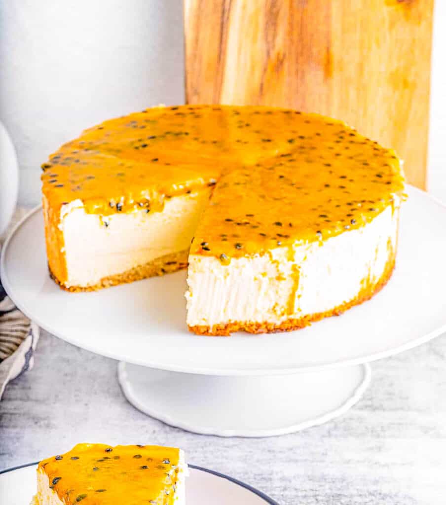 Slice of passionfruit cheesecake on a plate with whole cheesecake in the background.