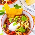 The best Instant Pot vegetarian chili, served in a bowl garnished with green onions, cheese, sour cream and tortilla chips.